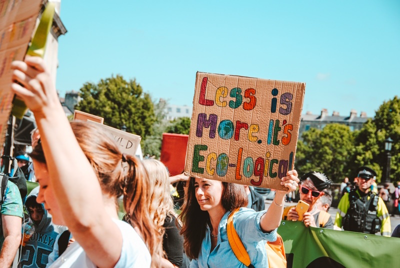 Person holding a sign that reads: 'Less is more. It's eco-logical.'