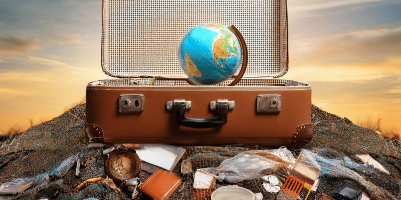 An open suitcase with the world in it, sitting on a pile of trash.